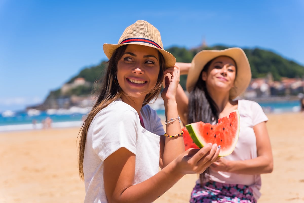 Portrait de deux amis en été sur la plage mangeant une pastèque avec la mer en arrière-plan